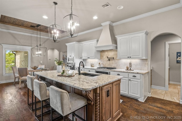 kitchen featuring custom exhaust hood, visible vents, arched walkways, an inviting chandelier, and a sink