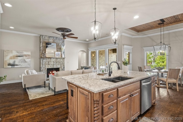 kitchen featuring ceiling fan with notable chandelier, stainless steel dishwasher, a fireplace, a sink, and brown cabinets