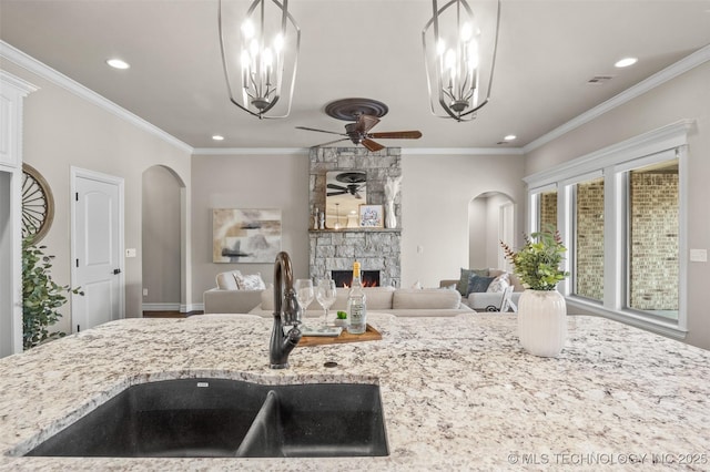 kitchen featuring ceiling fan with notable chandelier, a fireplace, arched walkways, recessed lighting, and a sink