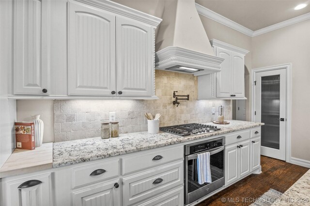 kitchen with custom range hood, ornamental molding, white cabinets, dark wood-type flooring, and appliances with stainless steel finishes