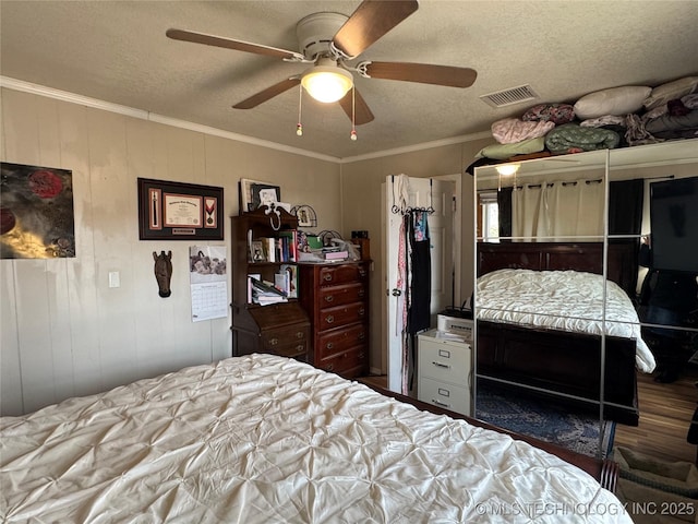 bedroom with wooden walls, ornamental molding, ceiling fan, a textured ceiling, and a closet