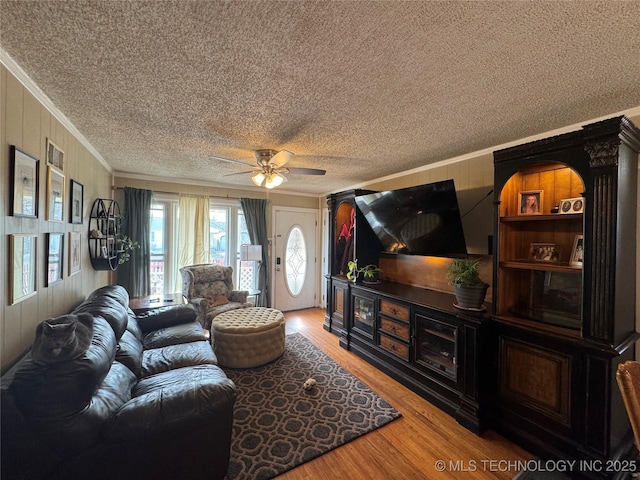 living room with crown molding, wood-type flooring, wooden walls, and ceiling fan