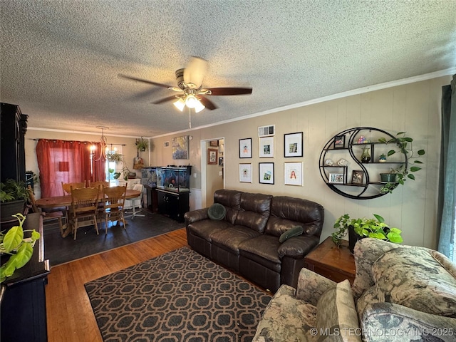 living room featuring dark hardwood / wood-style flooring, ceiling fan with notable chandelier, ornamental molding, and a textured ceiling