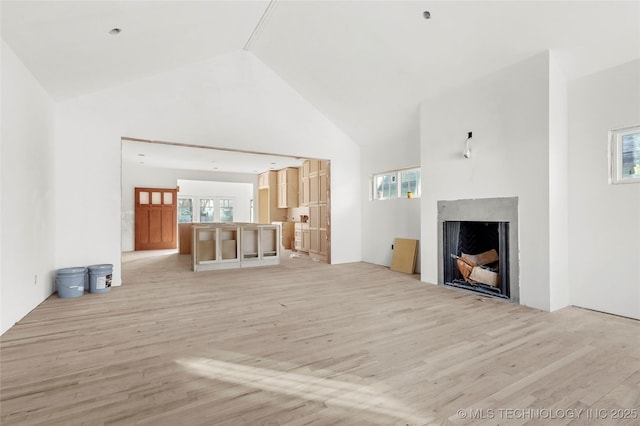 unfurnished living room with high vaulted ceiling, a healthy amount of sunlight, and light hardwood / wood-style floors