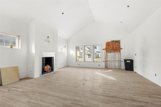 unfurnished living room with high vaulted ceiling, a healthy amount of sunlight, and light wood-type flooring