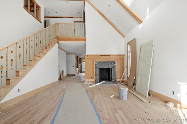 unfurnished living room with high vaulted ceiling, a tiled fireplace, and light hardwood / wood-style floors