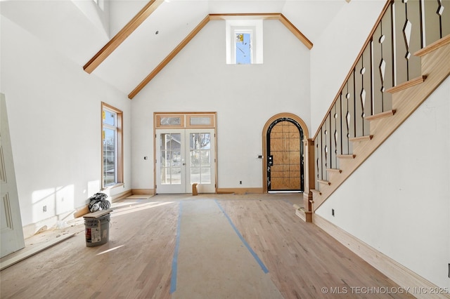 unfurnished living room featuring french doors, light hardwood / wood-style flooring, and a towering ceiling