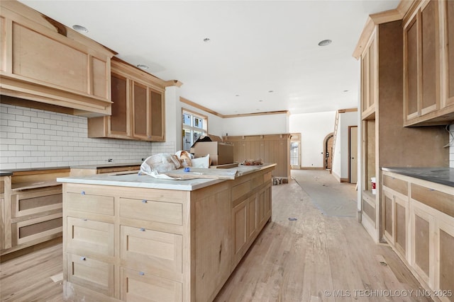 kitchen featuring light brown cabinets, backsplash, ornamental molding, a kitchen island, and light hardwood / wood-style flooring