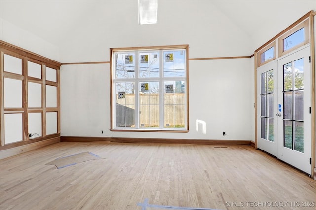 unfurnished room featuring light wood-type flooring, a healthy amount of sunlight, french doors, and high vaulted ceiling