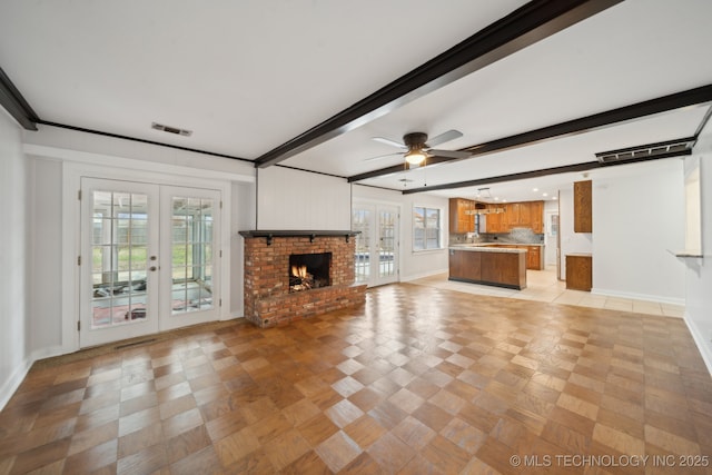 unfurnished living room with a fireplace, beam ceiling, french doors, and ceiling fan