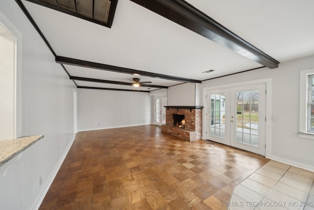 unfurnished living room featuring french doors, beamed ceiling, ceiling fan, a brick fireplace, and light parquet floors