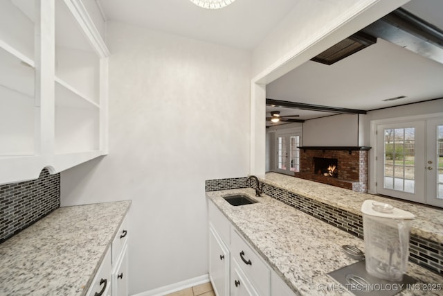 kitchen with decorative backsplash, sink, white cabinetry, light stone countertops, and french doors