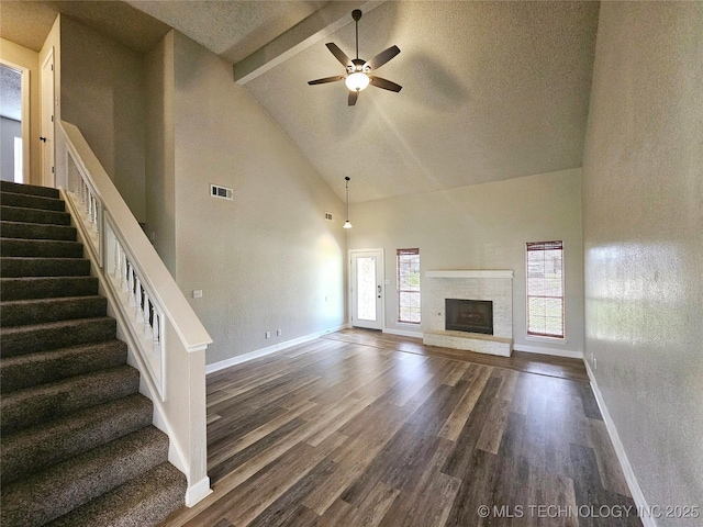 unfurnished living room with ceiling fan, dark wood-type flooring, a fireplace, high vaulted ceiling, and beam ceiling