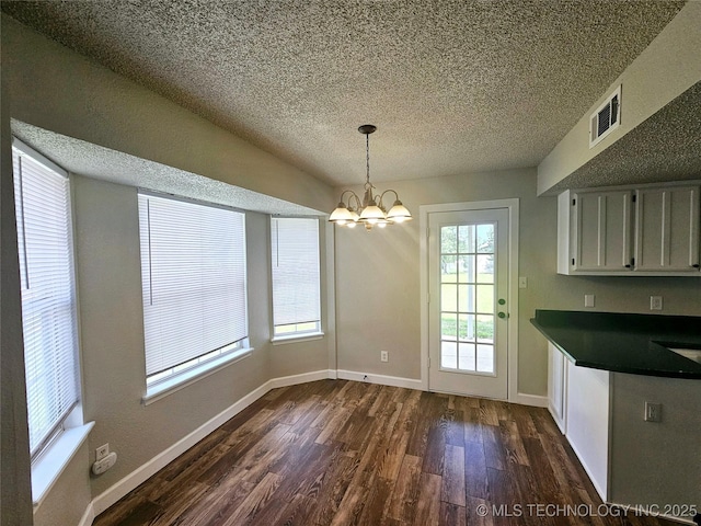 unfurnished dining area featuring a textured ceiling, a chandelier, and dark hardwood / wood-style floors