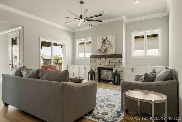 living room featuring ceiling fan, wood-type flooring, crown molding, and a stone fireplace