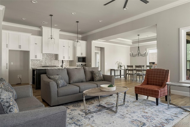 living room featuring ceiling fan with notable chandelier, light hardwood / wood-style flooring, and ornamental molding