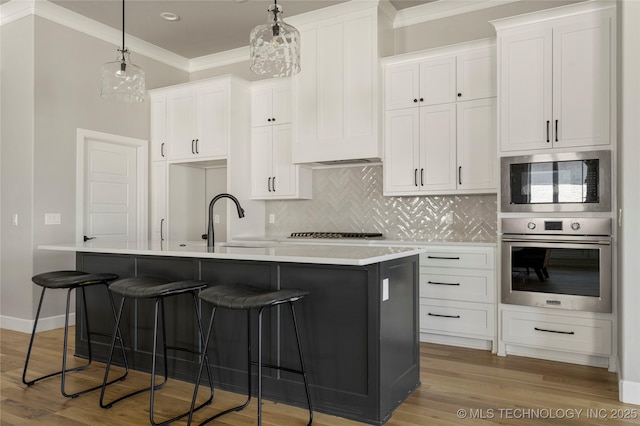 kitchen with white cabinets, ornamental molding, stainless steel appliances, and a center island with sink