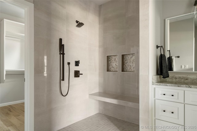 bathroom with hardwood / wood-style flooring, tiled shower, and vanity