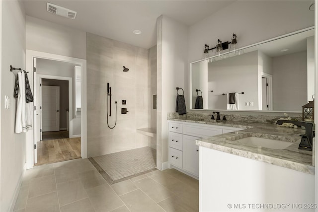 bathroom featuring tile patterned flooring, a tile shower, and vanity