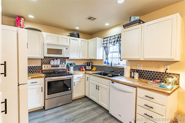 kitchen featuring white appliances, white cabinetry, butcher block counters, light hardwood / wood-style floors, and sink