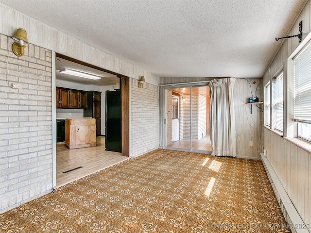 unfurnished living room featuring brick wall, baseboard heating, a textured ceiling, and wooden walls