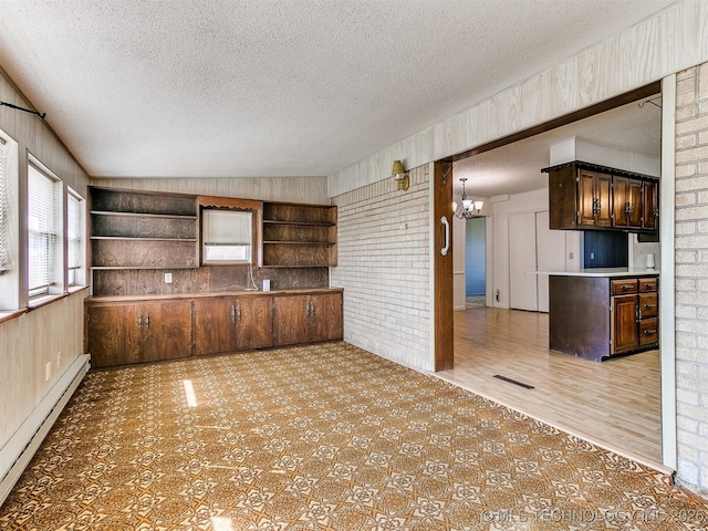 kitchen featuring a baseboard radiator, brick wall, a textured ceiling, an inviting chandelier, and dark brown cabinets