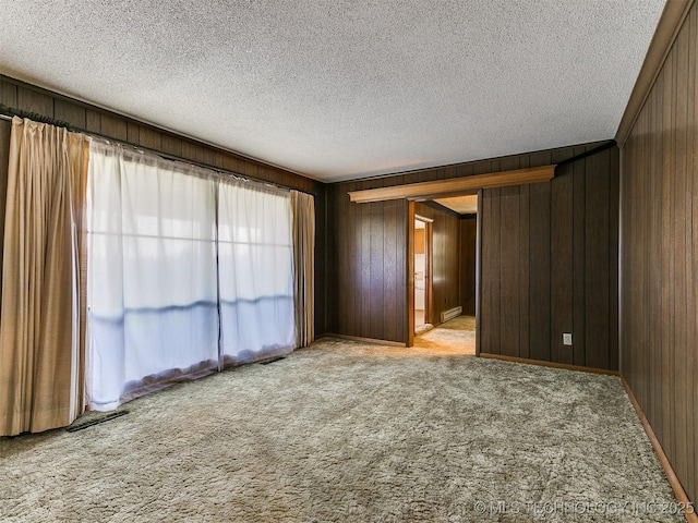 spare room with light colored carpet, a textured ceiling, and wooden walls