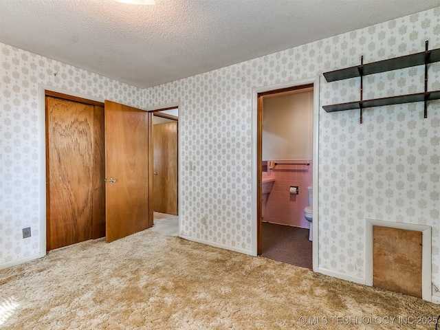 unfurnished bedroom with light colored carpet, a textured ceiling, and ensuite bathroom