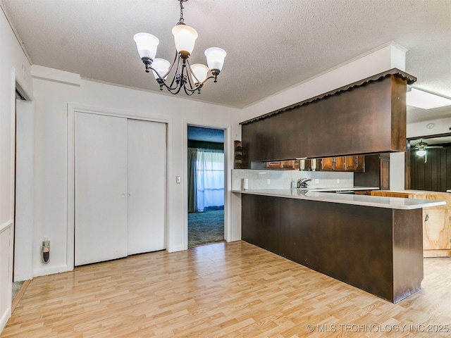 kitchen featuring light hardwood / wood-style floors, pendant lighting, kitchen peninsula, a textured ceiling, and dark brown cabinets