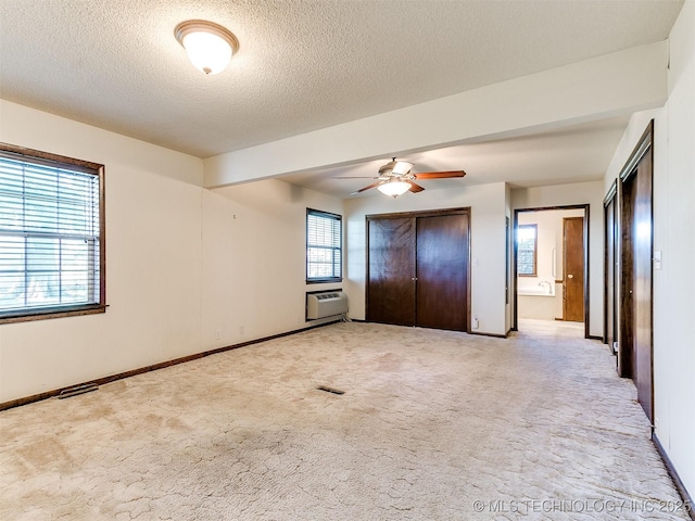 unfurnished bedroom featuring ceiling fan, a wall mounted air conditioner, connected bathroom, a textured ceiling, and light carpet