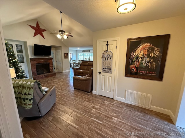 living room with hardwood / wood-style flooring, a brick fireplace, ceiling fan, and lofted ceiling