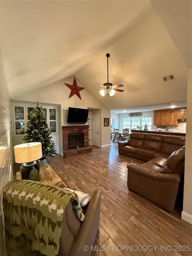 living room featuring light wood-type flooring, vaulted ceiling, ceiling fan, and a fireplace