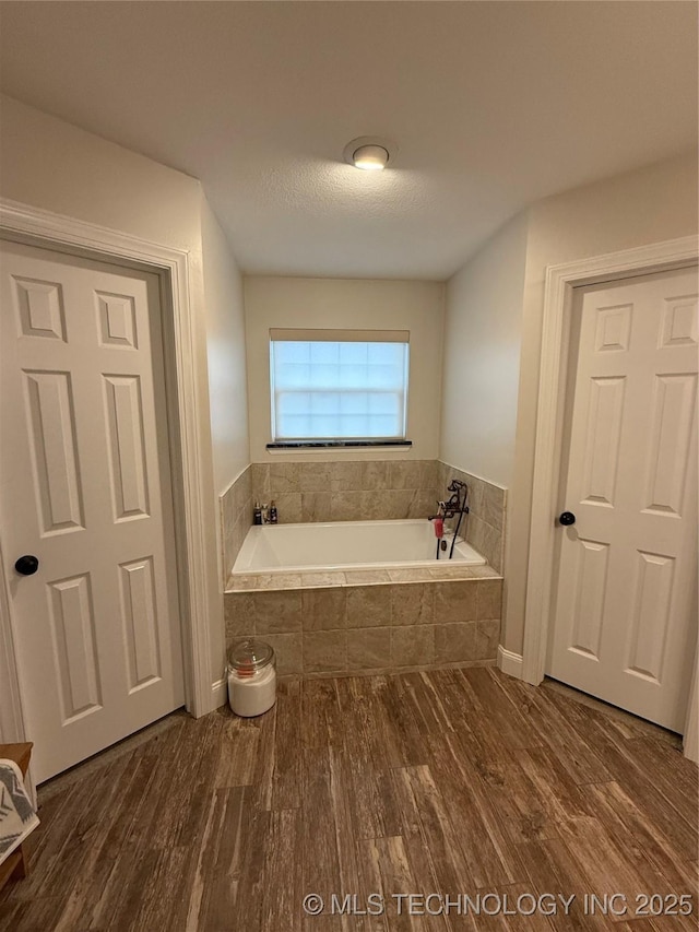 bathroom with tiled bath and hardwood / wood-style flooring