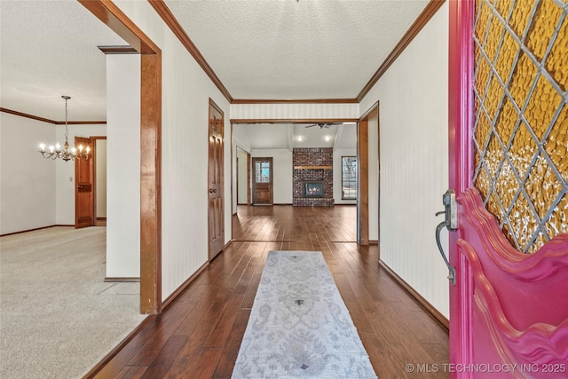 entryway with crown molding, a textured ceiling, a brick fireplace, an inviting chandelier, and dark hardwood / wood-style flooring