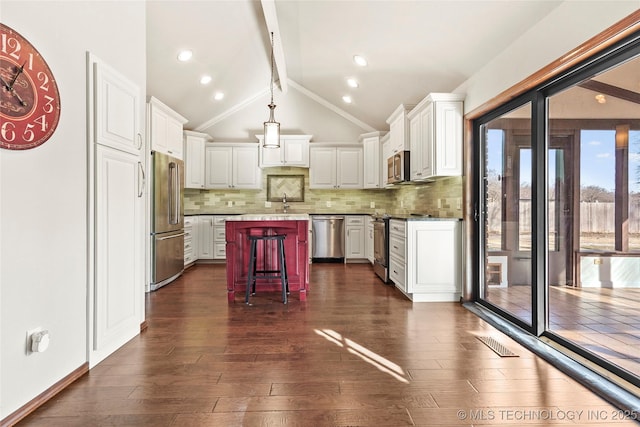 kitchen with appliances with stainless steel finishes, a kitchen island, white cabinetry, lofted ceiling with beams, and a breakfast bar