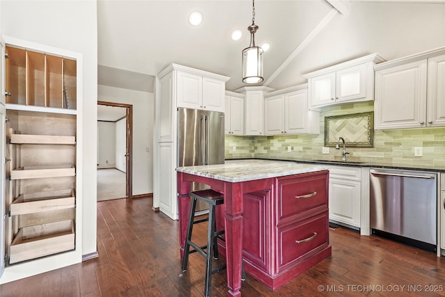 kitchen with appliances with stainless steel finishes, white cabinetry, sink, dark stone countertops, and lofted ceiling with beams