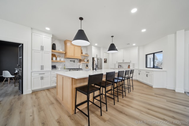 kitchen featuring decorative light fixtures, white cabinetry, decorative backsplash, light hardwood / wood-style floors, and a center island with sink