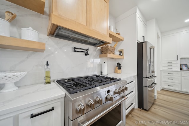 kitchen featuring light stone countertops, white cabinetry, high end appliances, light hardwood / wood-style floors, and backsplash