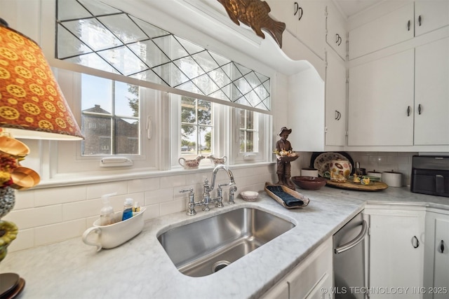 kitchen with backsplash, white cabinets, light stone counters, and sink