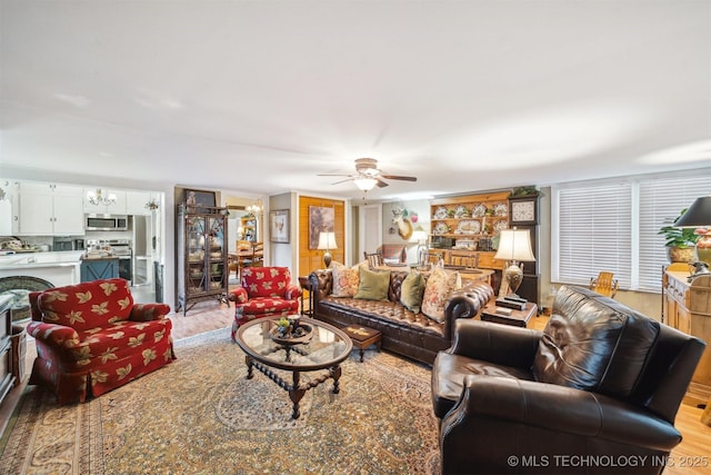 living room with ceiling fan with notable chandelier and light hardwood / wood-style floors