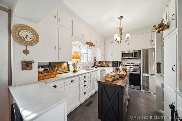 kitchen featuring white cabinets, a kitchen island, stainless steel appliances, sink, and hanging light fixtures