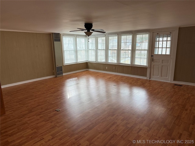 empty room featuring hardwood / wood-style flooring, a wealth of natural light, wood walls, and ceiling fan