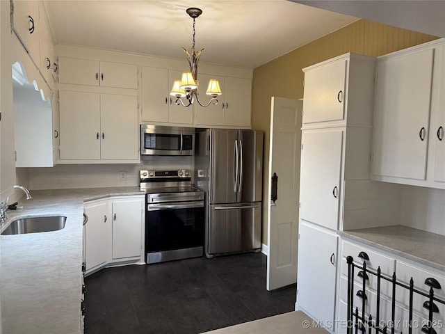 kitchen with stainless steel appliances, hanging light fixtures, a chandelier, white cabinets, and sink