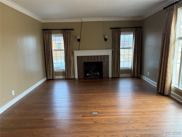 unfurnished living room featuring a healthy amount of sunlight, a tiled fireplace, ornamental molding, and hardwood / wood-style flooring