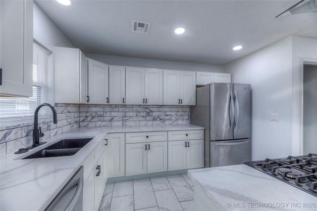 kitchen with decorative backsplash, sink, white cabinetry, light stone countertops, and stainless steel appliances