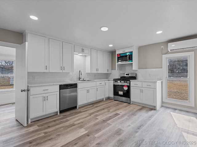 kitchen with sink, white cabinetry, a wall mounted air conditioner, light wood-type flooring, and appliances with stainless steel finishes