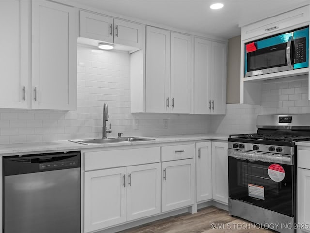 kitchen featuring white cabinets, appliances with stainless steel finishes, sink, backsplash, and light wood-type flooring