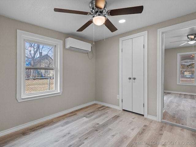 unfurnished bedroom featuring a wall unit AC, ceiling fan, and light wood-type flooring