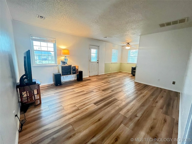 living room featuring ceiling fan, hardwood / wood-style flooring, a wealth of natural light, and a textured ceiling