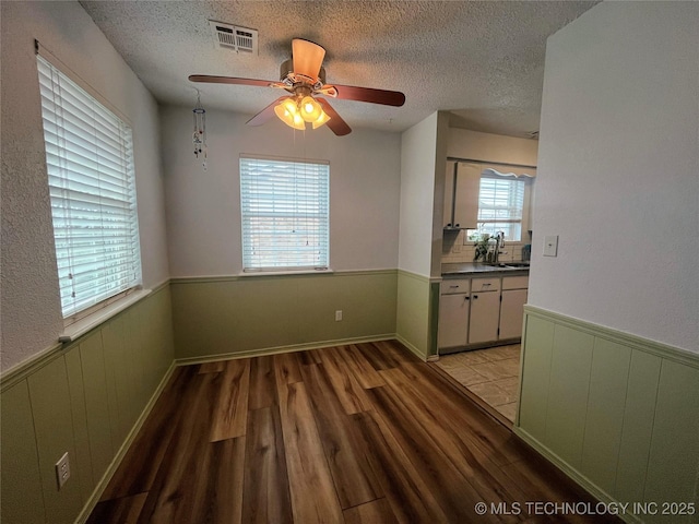 unfurnished dining area with ceiling fan, sink, light hardwood / wood-style flooring, and a textured ceiling